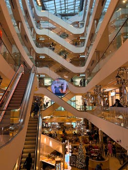 Vertical view of a bustling multi-level shopping mall with escalators and festive decorations.